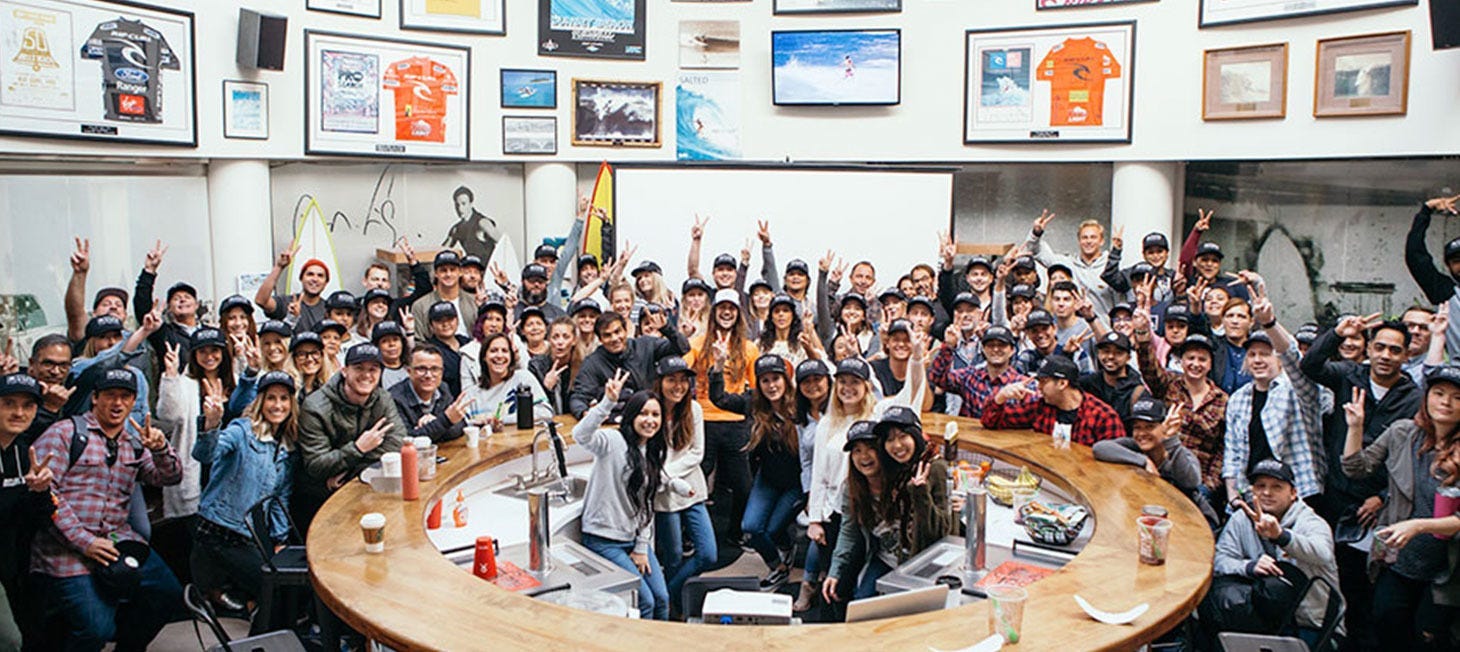 Massive crowd of Rip Curl Crew, throwing up the peace sign, in a wide circular room