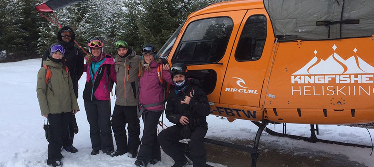 Rip Curl crew in snow gear, posing by a helicopter that has landed in the snow