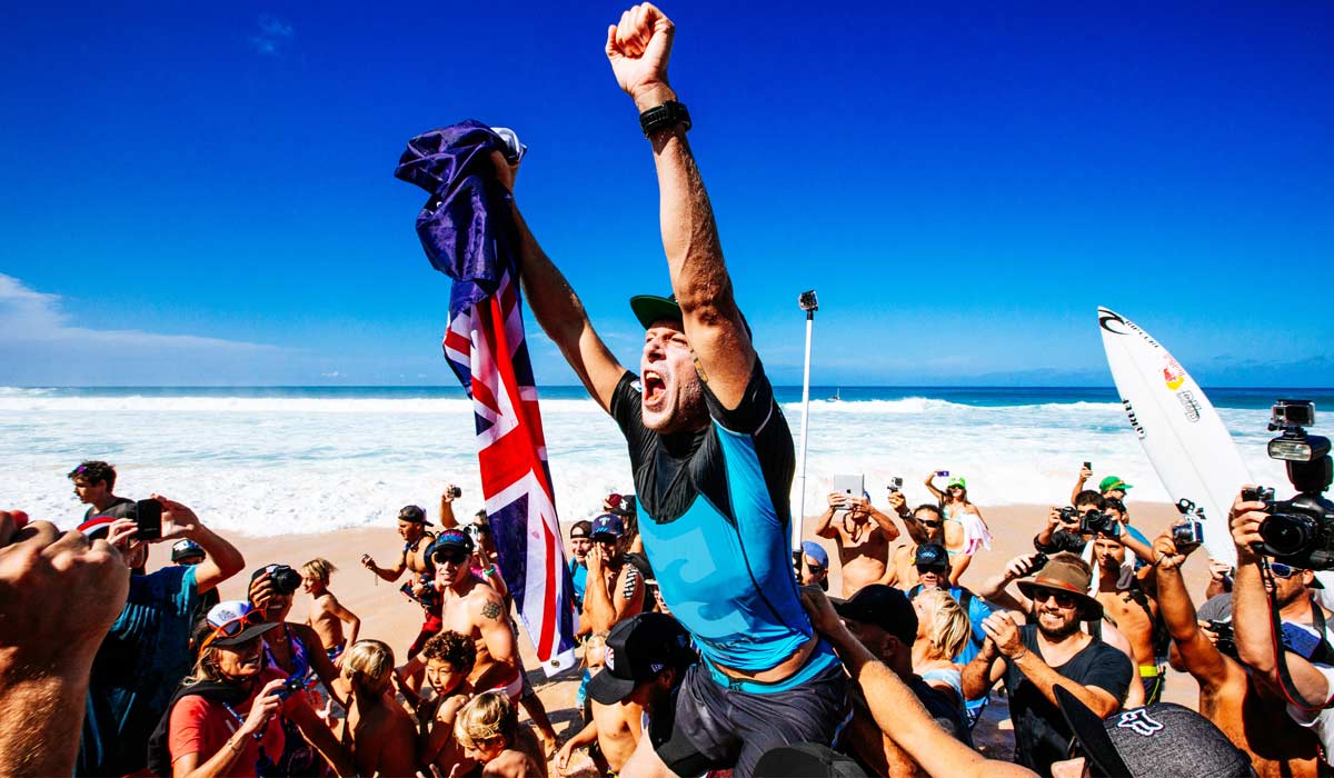Mick Fanning being chaired across the beach, fans and media celebrating behind him