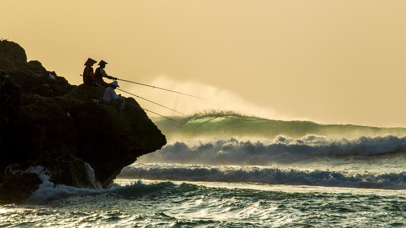 Two fisherman sitting on a rock at Padang Padang surf break