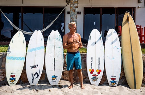 Tom Curren standing in between surfboards