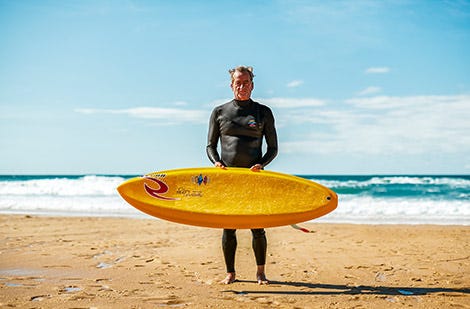 Tom Curren holding his surfboard on the beach